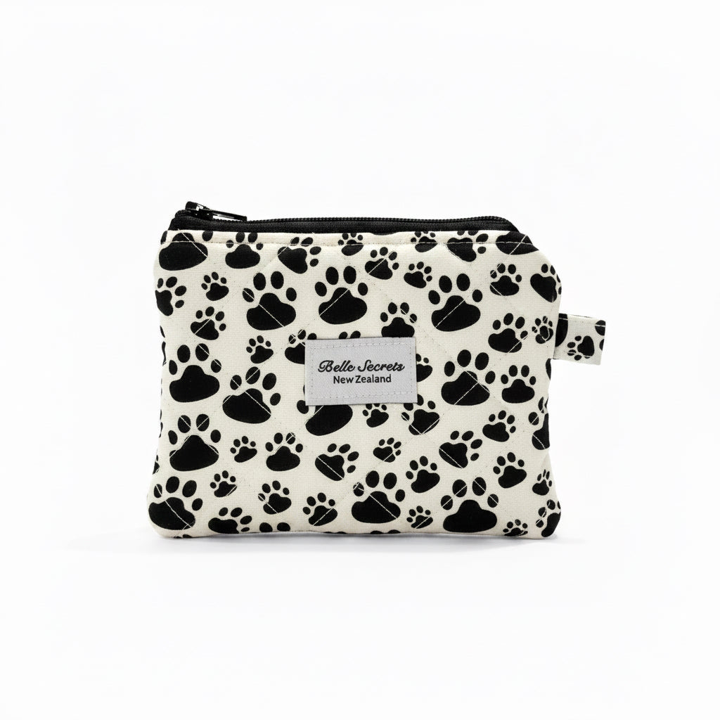 A small zippered pouch with a black paw print pattern on a white background, featuring a white label that reads 'Belle Secrets' and 'New Zealand'.