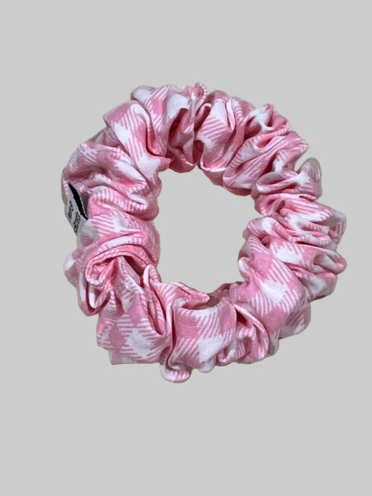 A pink and white patterned fabric scrunchie resting on a textured beige linen background.