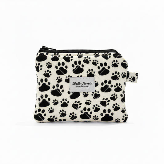 A small zippered pouch with a black paw print pattern on a white background, featuring a white label that reads 'Belle Secrets' and 'New Zealand'.